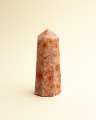 A polished, pink sunstone crystal with a pointed top, displayed against a neutral background.