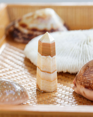 A banded calcite mini gemstone tower with a light yellow hue, placed on a bamboo mat alongside other decorative items.