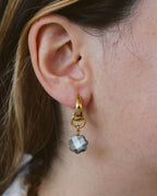 Closeup of woman wearing gold-colored hoop earrings with interchangeable mother of pearl charm.