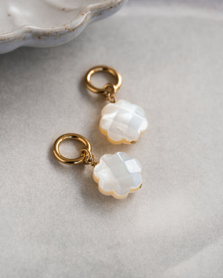A pair of gold-colored hoop earrings with interchangeable mother of pearl charms displayed on a piece of paper.