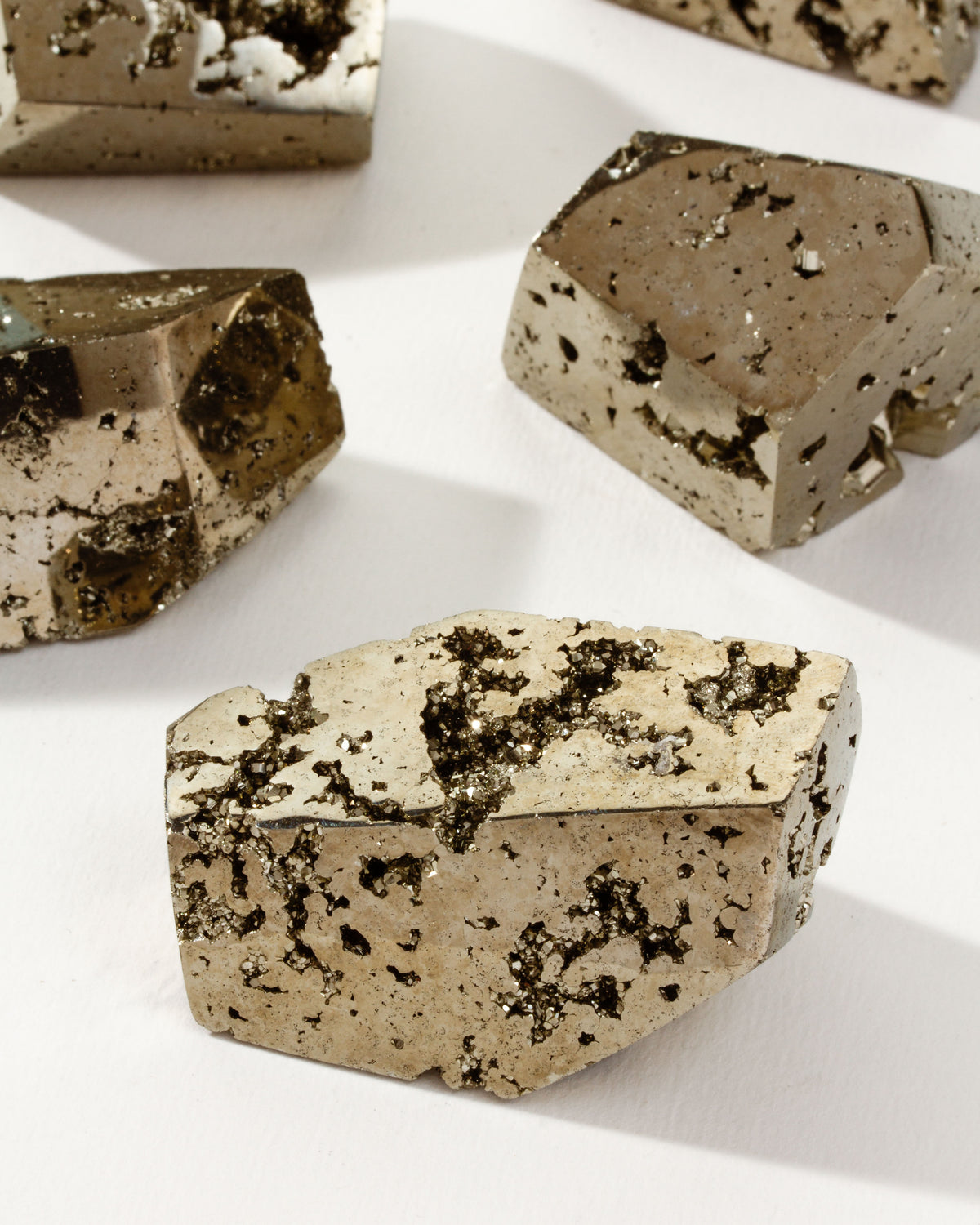 A collection of freeform faceted pyrite stones displayed on a white surface.