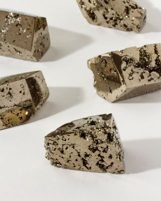 several geometric cut gold, hue pyrite gemstones on a white surface.