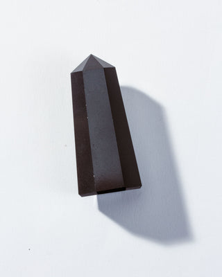A faceted, polished black onyx gemstone in a pointed tower shape against a white background.