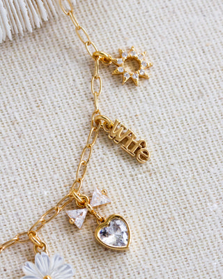 Closeup of gold necklace with sun, floral, Wife, and heart charms on a textured beige background