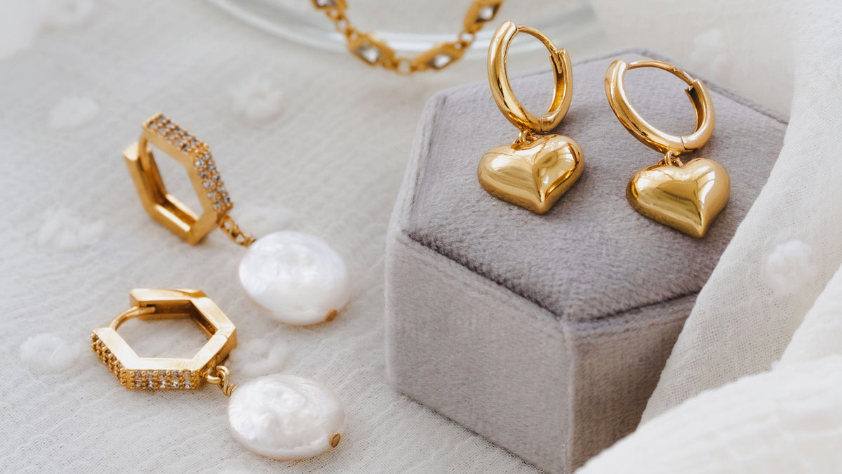 Gold heart shaped earrings and on a textured surface with a jewelry box.