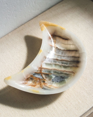 A moon-shaped catch-all dish, carved from genuine multicolored calcite, displayed on a light background with shadows.