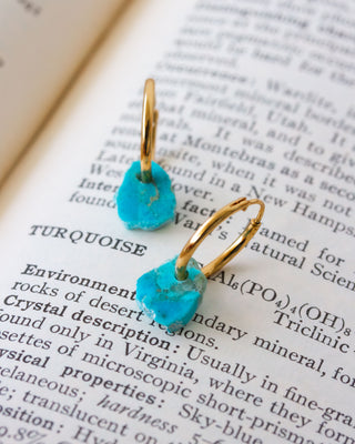 Turquoise earrings with gold hoops on an open book.