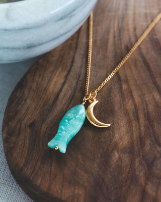 Necklace with a turquoise fish pendant and gold crescent moon on a wooden surface
