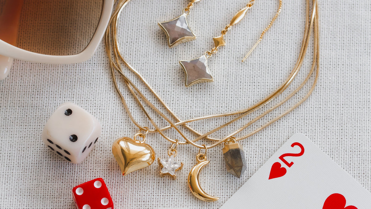 Gold necklaces with charms on a textured surface with dice and playing cards.