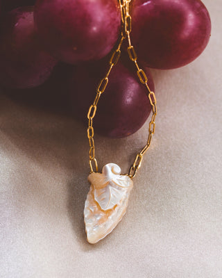 A necklace with a grape pendant made of mother of pearl, displayed on table.