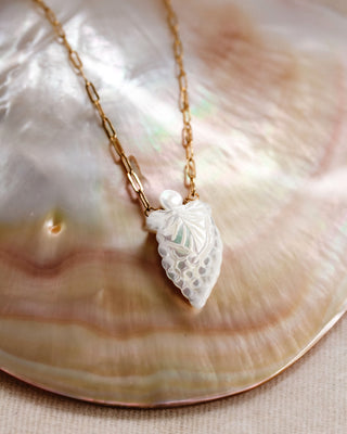 A necklace with a grape pendant made of mother of pearl, displayed on a shell.