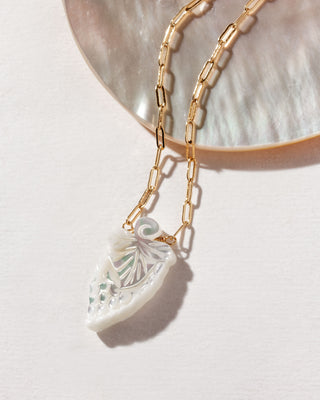 A necklace with a grape pendant made of mother of pearl, displayed on a shell.