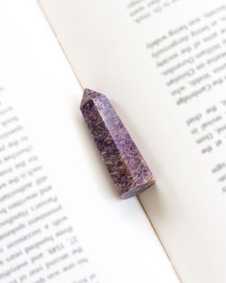 A faceted lepidolite crystal tower with lilac and purple tones, placed on an open book.