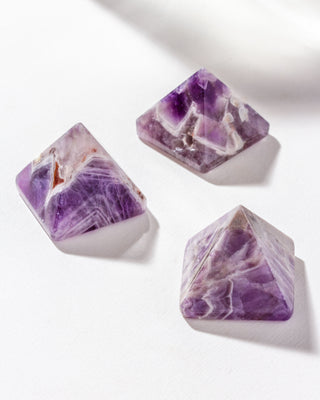 Three amethyst pyramid gemstone curios sitting on a white surface.