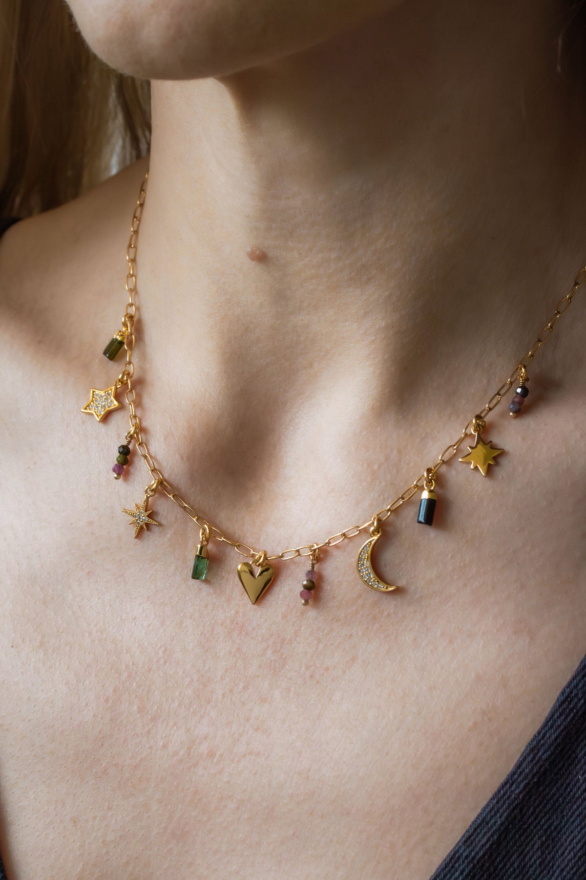 Woman wearing delicate gold plated charm chain necklace with many different charms.