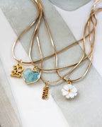 Gold necklaces with various pendants, including aquamarine heart, 2025, Wife, and mother of pearl floral charms, on a light fabric background.