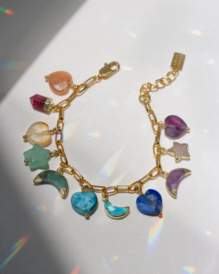 Gold bracelet with many different colorful gemstone heart, moon, and star charms on a white surface