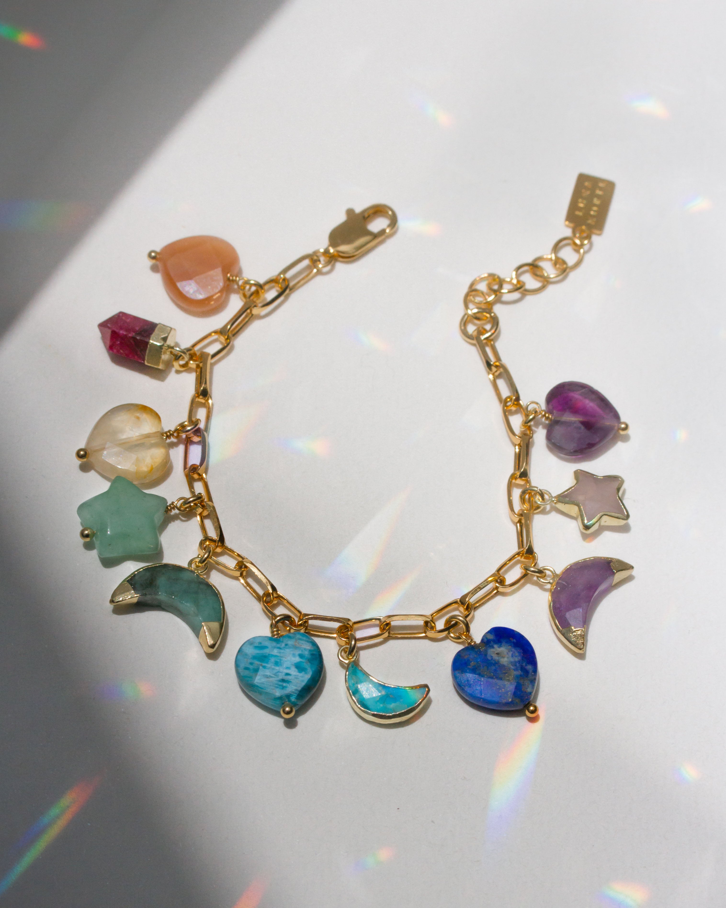 Gold bracelet with many different colorful gemstone heart, moon, and star charms on a white surface