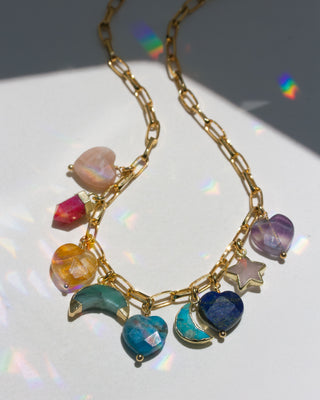 Gold necklace with many colorful heart, star, and moon gemstone charms on a reflective surface