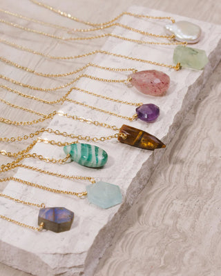 Gold necklaces with various shapes of colored gemstones on a textured surface
