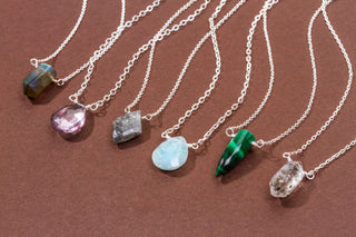 Examples of silver necklaces with various shapes and colorful gemstone pendants on a brown background