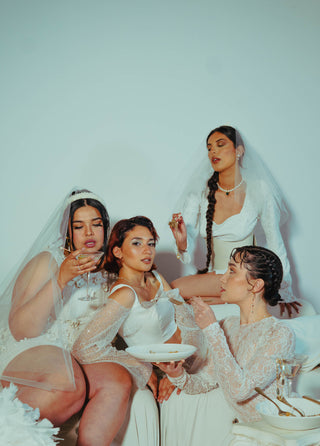 Four brides and bridesmaids in white posing together in a white room.