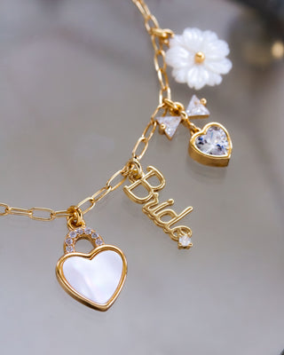 Gold bracelet with heart-shaped charm and 'Bride' word charm on a blurred background