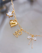 Gold necklace with heart, star, 2025 charm, and bow-shaped charms on a blurred background
