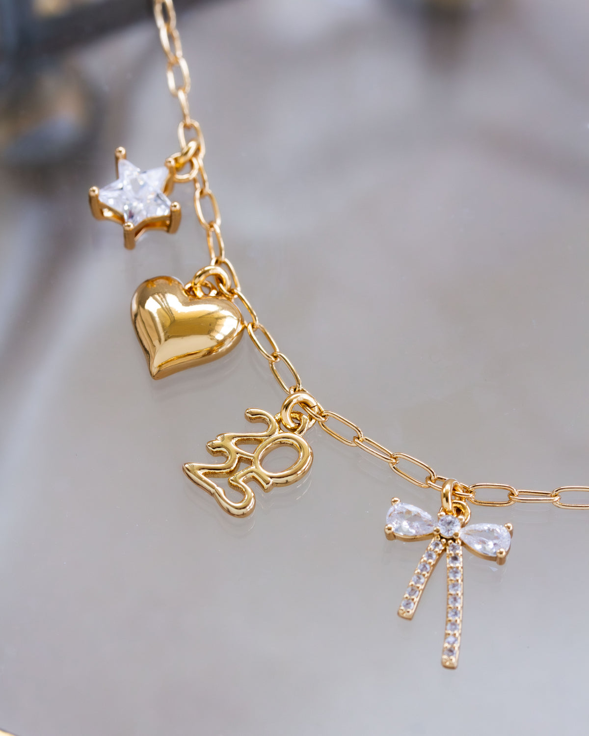 Gold necklace with heart, star, 2025 charm, and bow-shaped charms on a blurred background