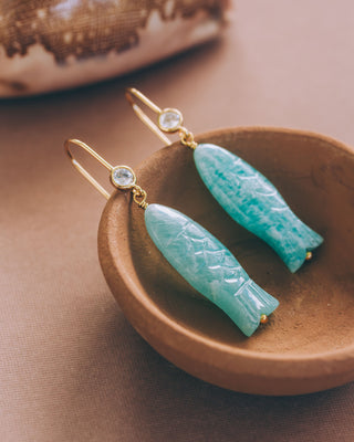 Turquoise fish earrings with gold accents on a brown dish