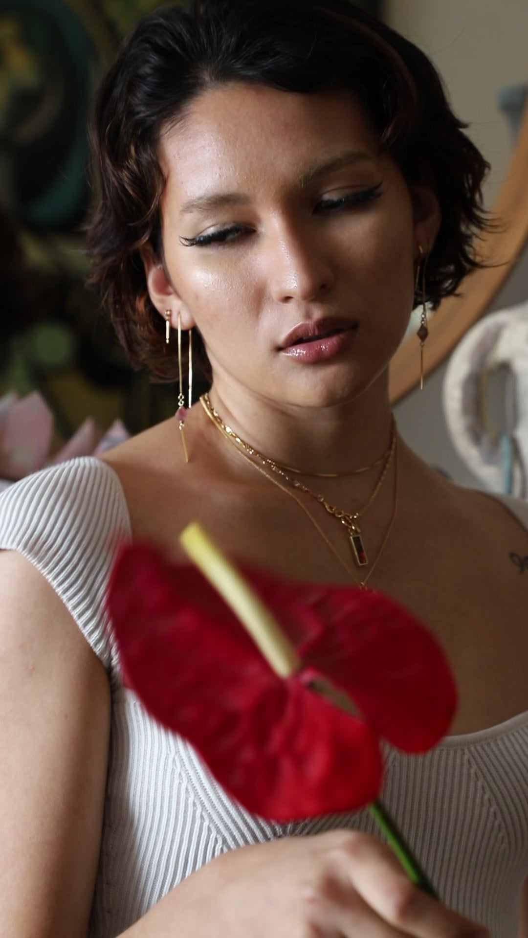 Person holding large red flower models various layered gold necklace and dangling earrings.