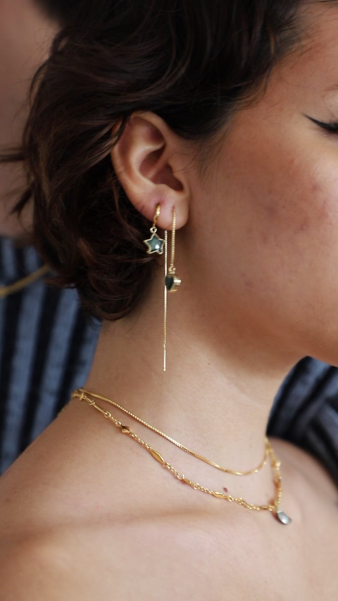 Person models many layered gold necklaces and charm earrings.