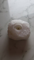 Closeup of white selenite candle being lit with a match, on a marble surface.