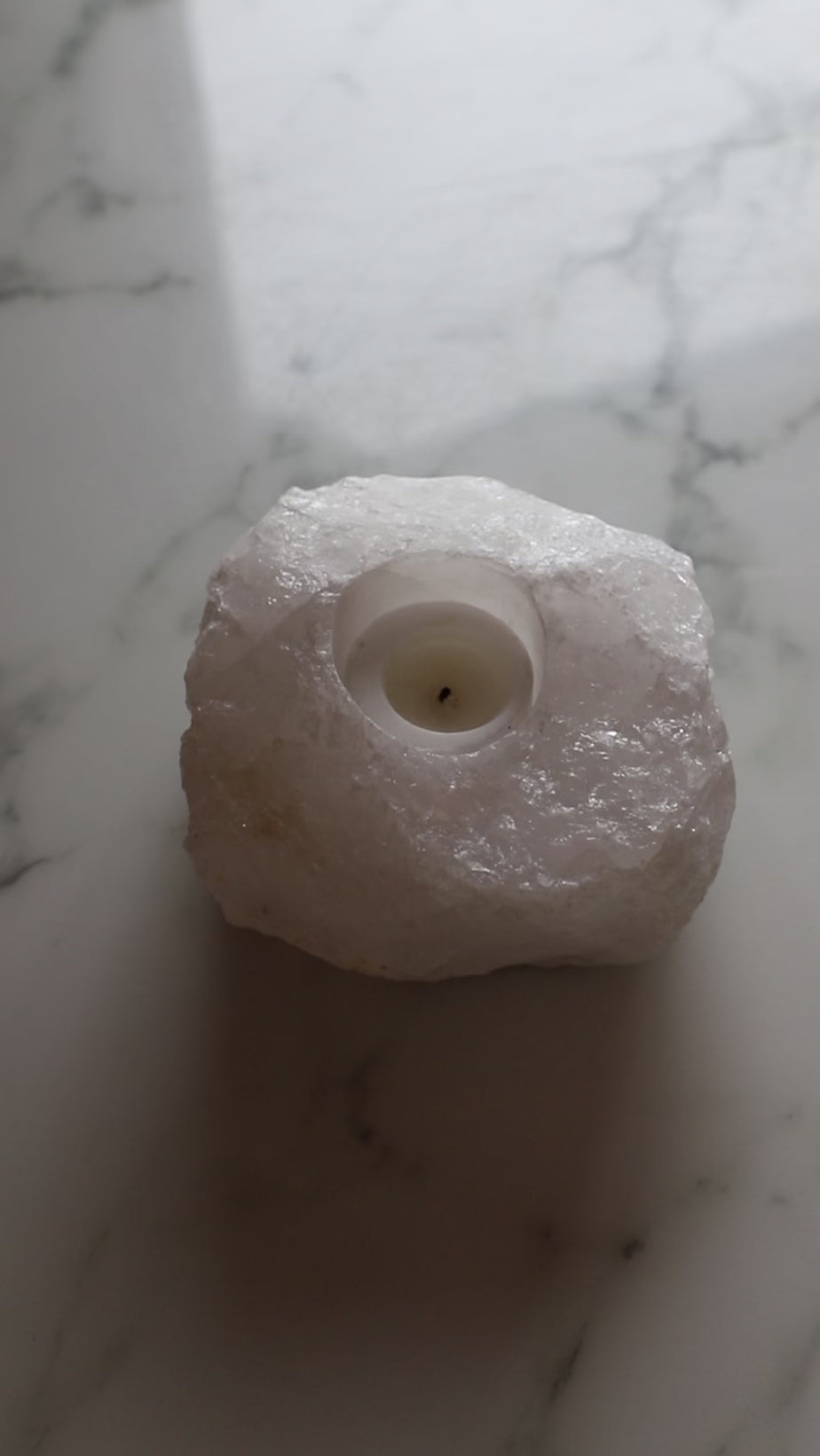 Closeup of white selenite candle being lit with a match, on a marble surface.