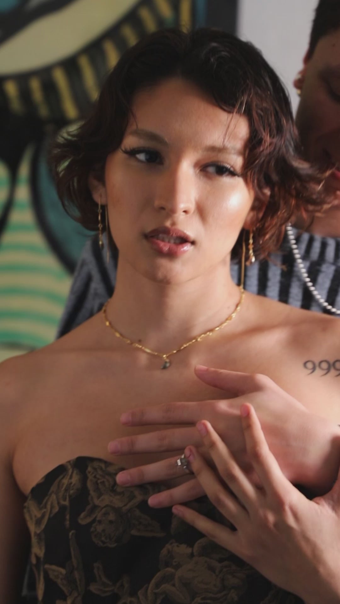 Two people in embrace with one wearing gold charm necklace and dangly earrings.