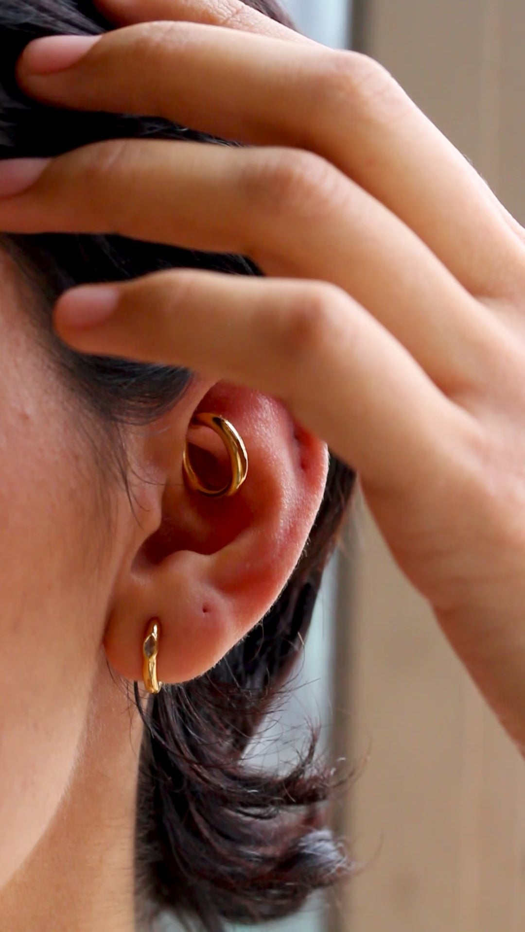 Closeup of persons ear with two gold small hoop earrings.