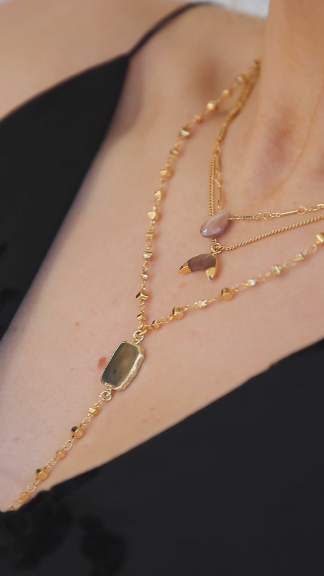 woman posing with several layered gold necklaces with different gemstone charms.