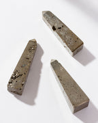 Three pyrite obelisk towers laying on a white surface.
