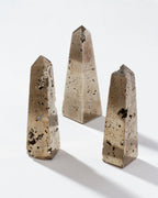 Three pyrite crystal obelisks with a gold-like hue, displayed against a white background.