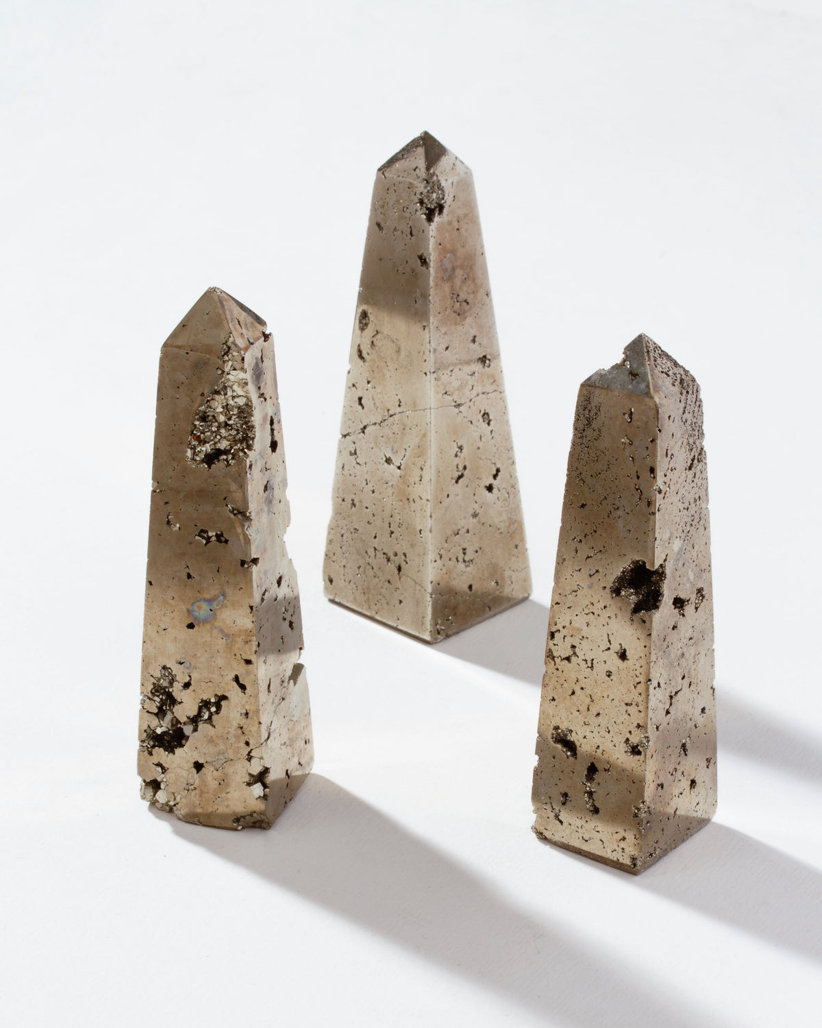 Three pyrite crystal obelisks with a gold-like hue, displayed against a white background.