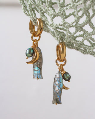 Close-up of the Tapas & Tides huggie hoop earring hanging from a fishing net; showcases the labradorite fish charm and bead.