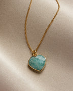 Amazonite heart-shaped pendant on a gold chain against a khaki cloth background