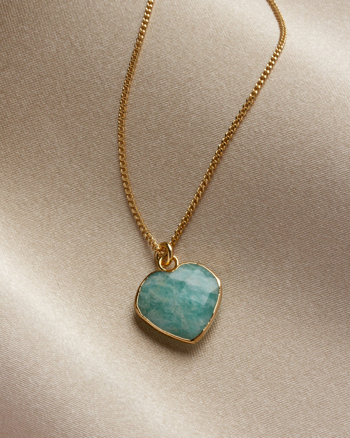 Amazonite heart-shaped pendant on a gold chain against a khaki cloth background