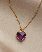 Close-up of amethyst heart-shaped charm necklace on a khaki background.