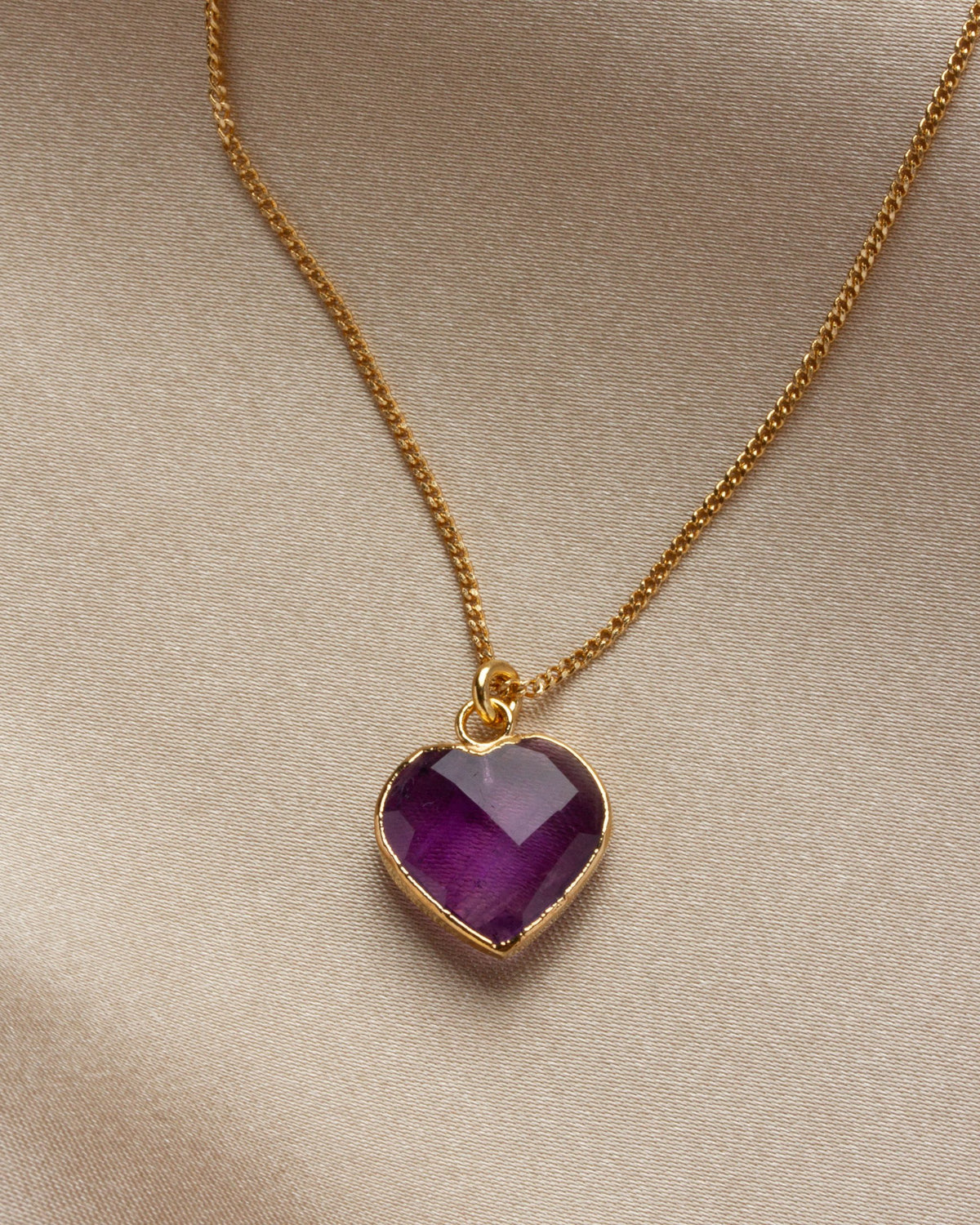 Close-up of amethyst heart-shaped charm necklace on a khaki background.