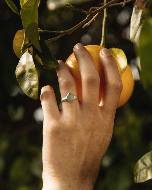 Hand holding an orange, wearing a sterling silver Aurora Labradorite ring.