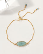 Adjustable gold bracelet featuring an aquamarine colored gemstone in a hexagon shape.