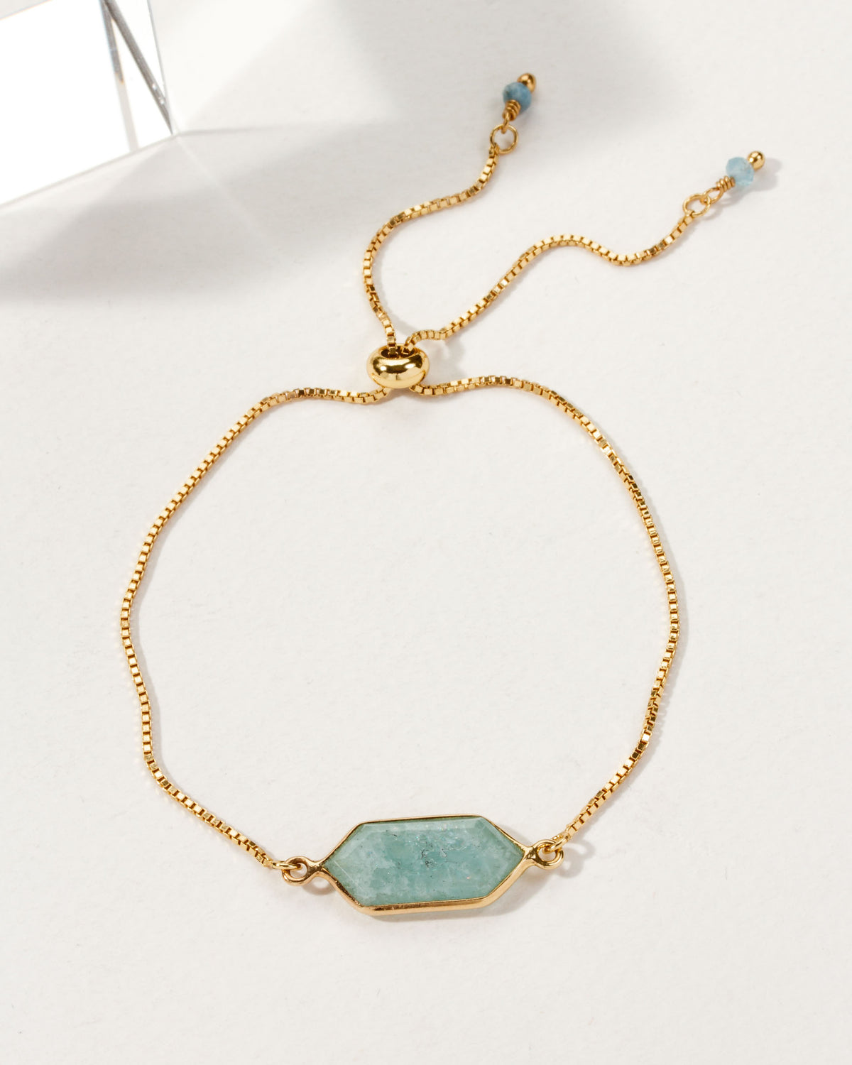 Adjustable gold bracelet featuring an aquamarine colored gemstone in a hexagon shape.