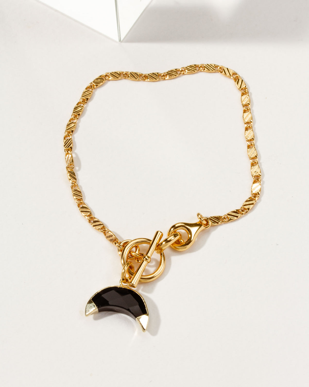 Gold chain bracelet with a crescent horn toggle featuring an onyx gemstone.