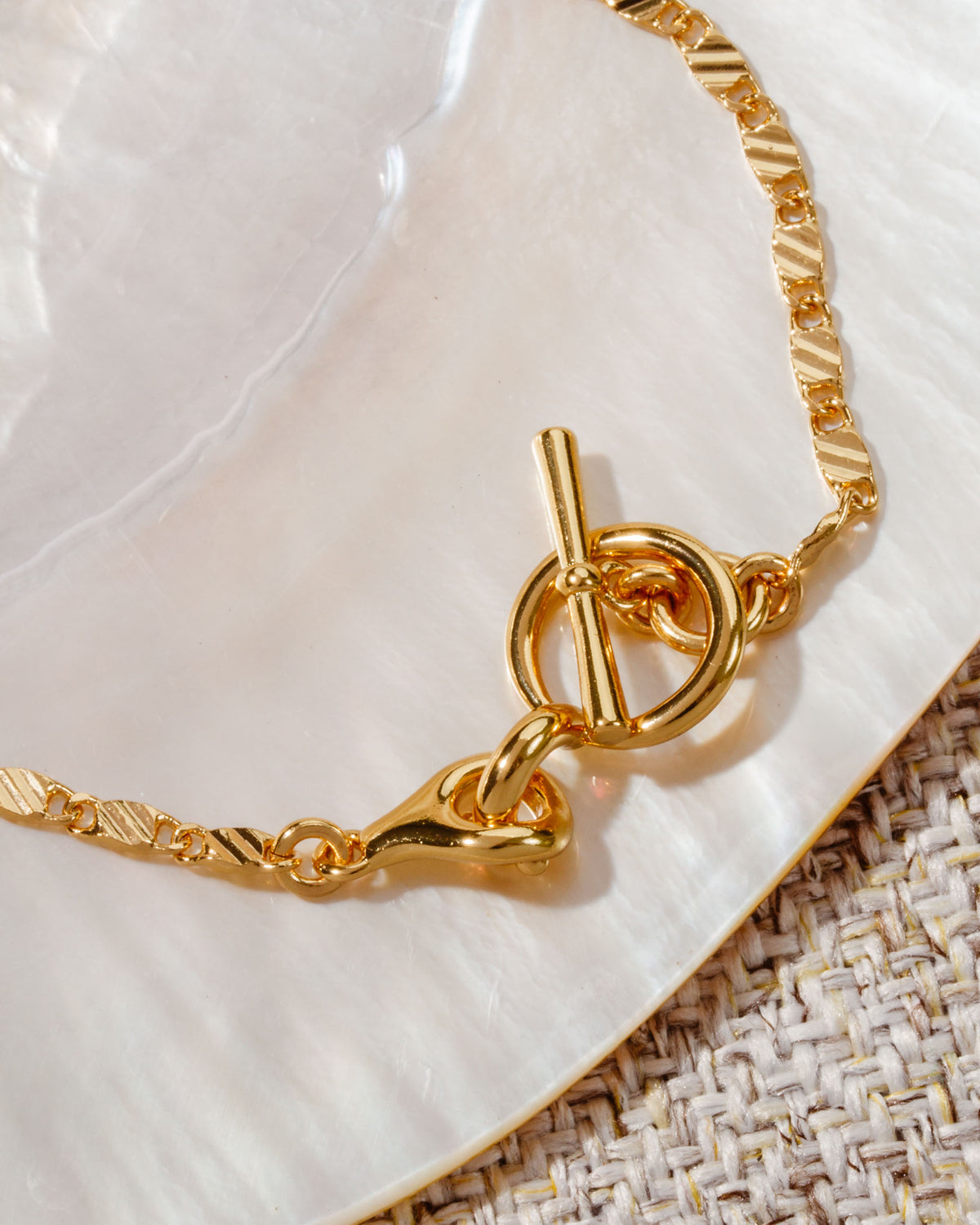 Gold plated Adorned Toggle Bracelet with bar and loop closure on a white and tan surface.